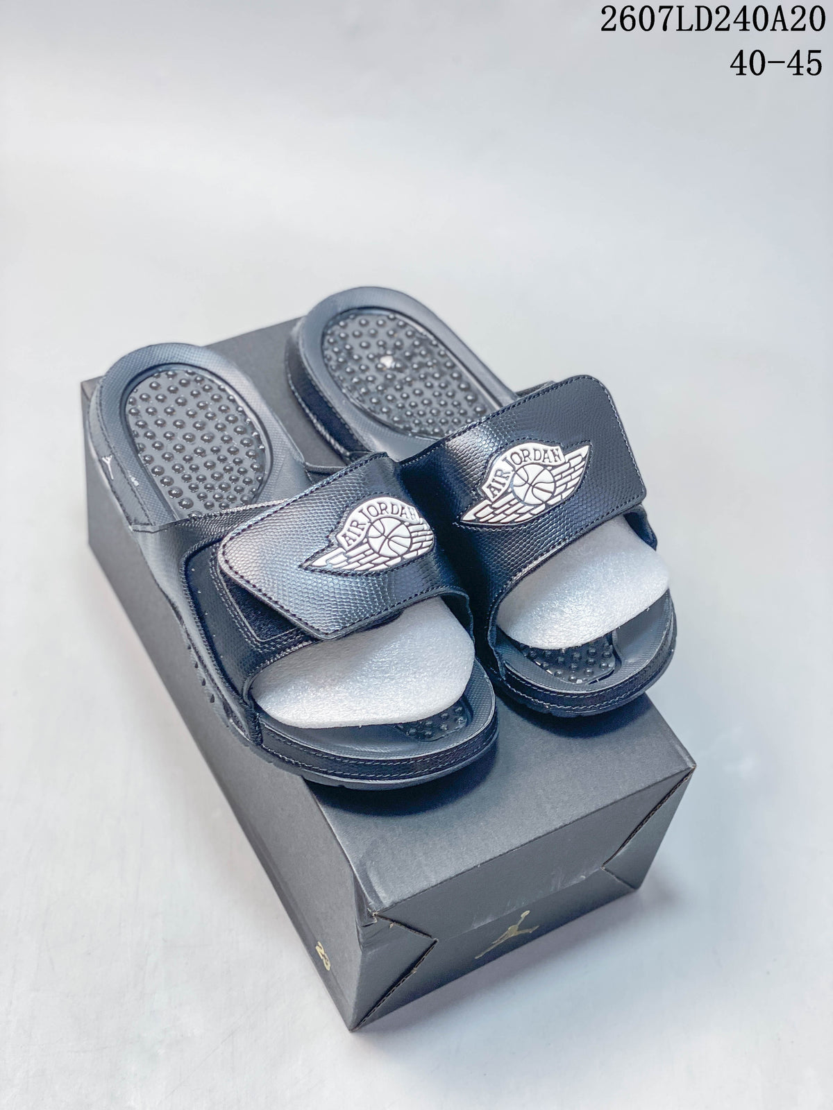 Pair of dark Jordan slides with adjustable straps displayed on a shoebox; image text shows style code 2607LD240A20 and size range 40–45.