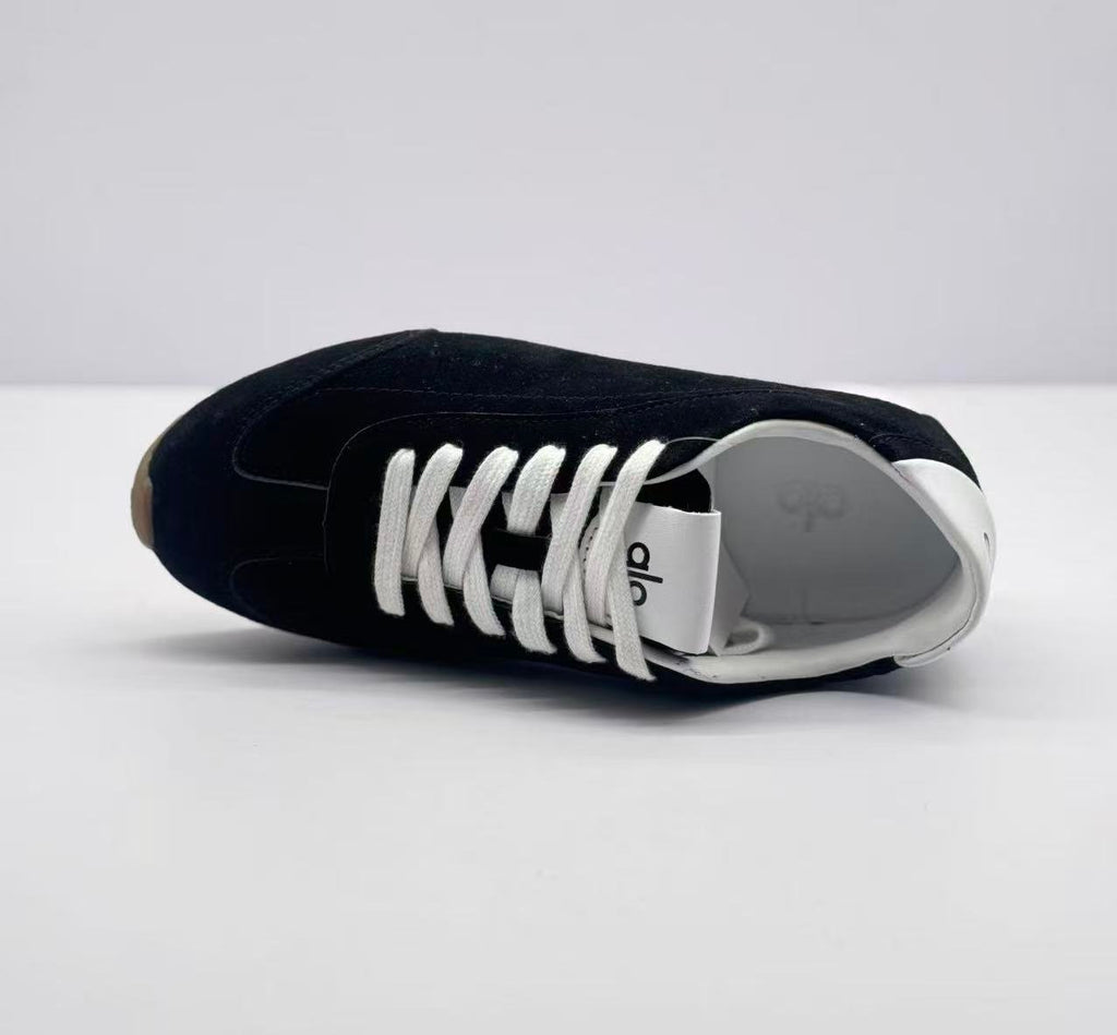 Top view of one black sneaker showing the lace arrangement, white tongue, and white interior.