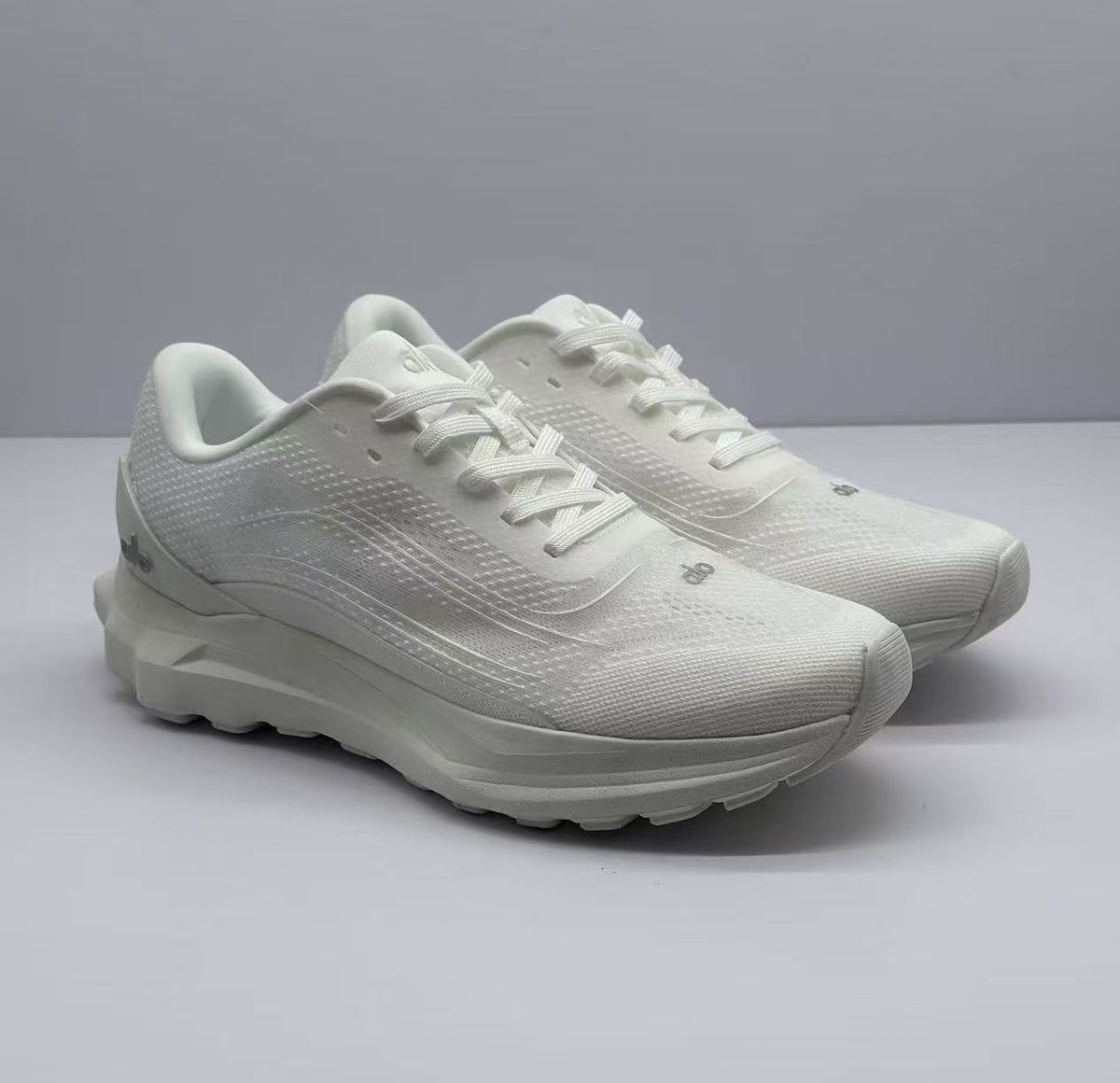 Pair of all-white Alo sneakers shown from a front three-quarter angle.