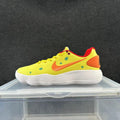 Side view of a yellow Nike low-top sneaker with an orange Swoosh and heel panel, green dots, red trim, and a white ridged-looking sole.