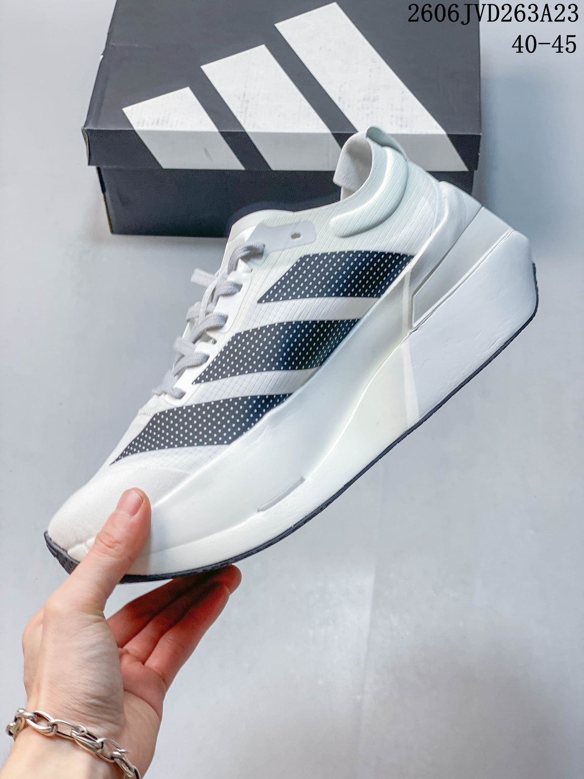 Side view of a white Adidas Adizero Dropset Elite shoe with dark dotted stripes and a sculpted midsole; image text shows sizes 40–45.