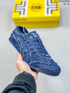 Close view of a blue denim-style low-top sneaker showing the lace area, side stripes, textured upper, and patterned outsole.