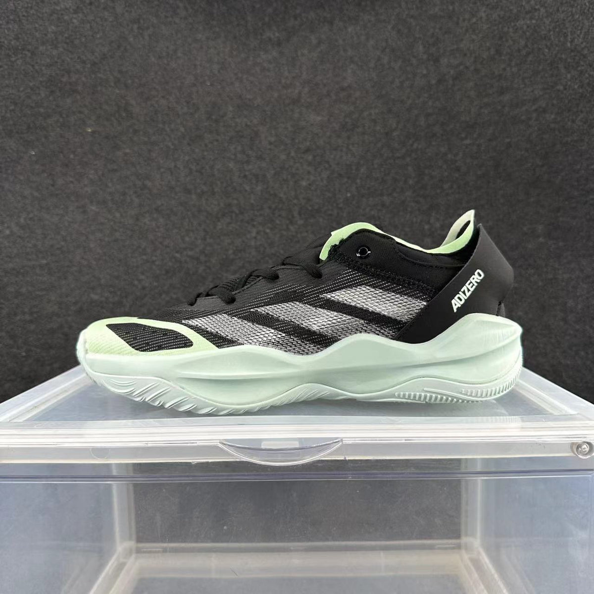 Side view of a black Adidas Adizero sneaker with light-colored stripes, pale green accents, and a light sculpted sole