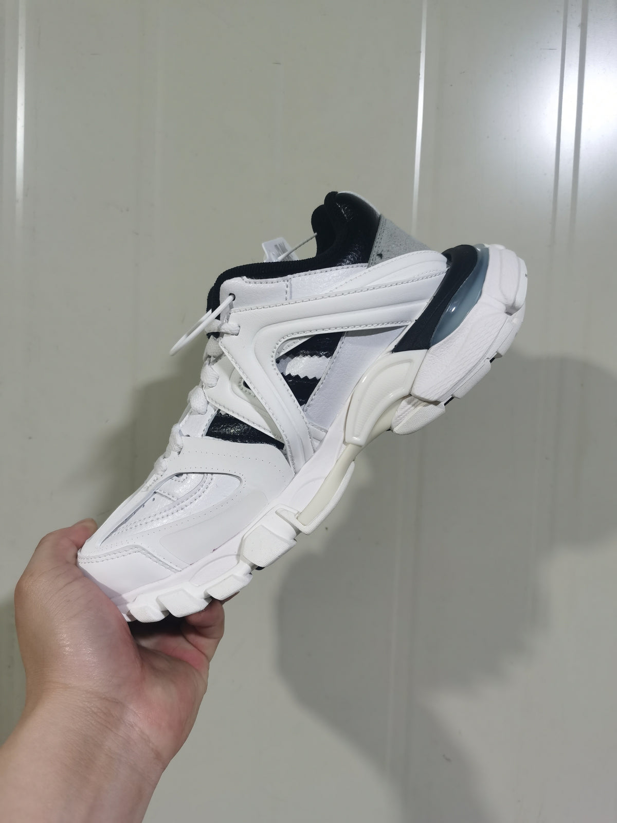 Side and top view of a white and black low-top sneaker showing layered panels, lace-up construction, dark accents and a chunky segmented outsole.