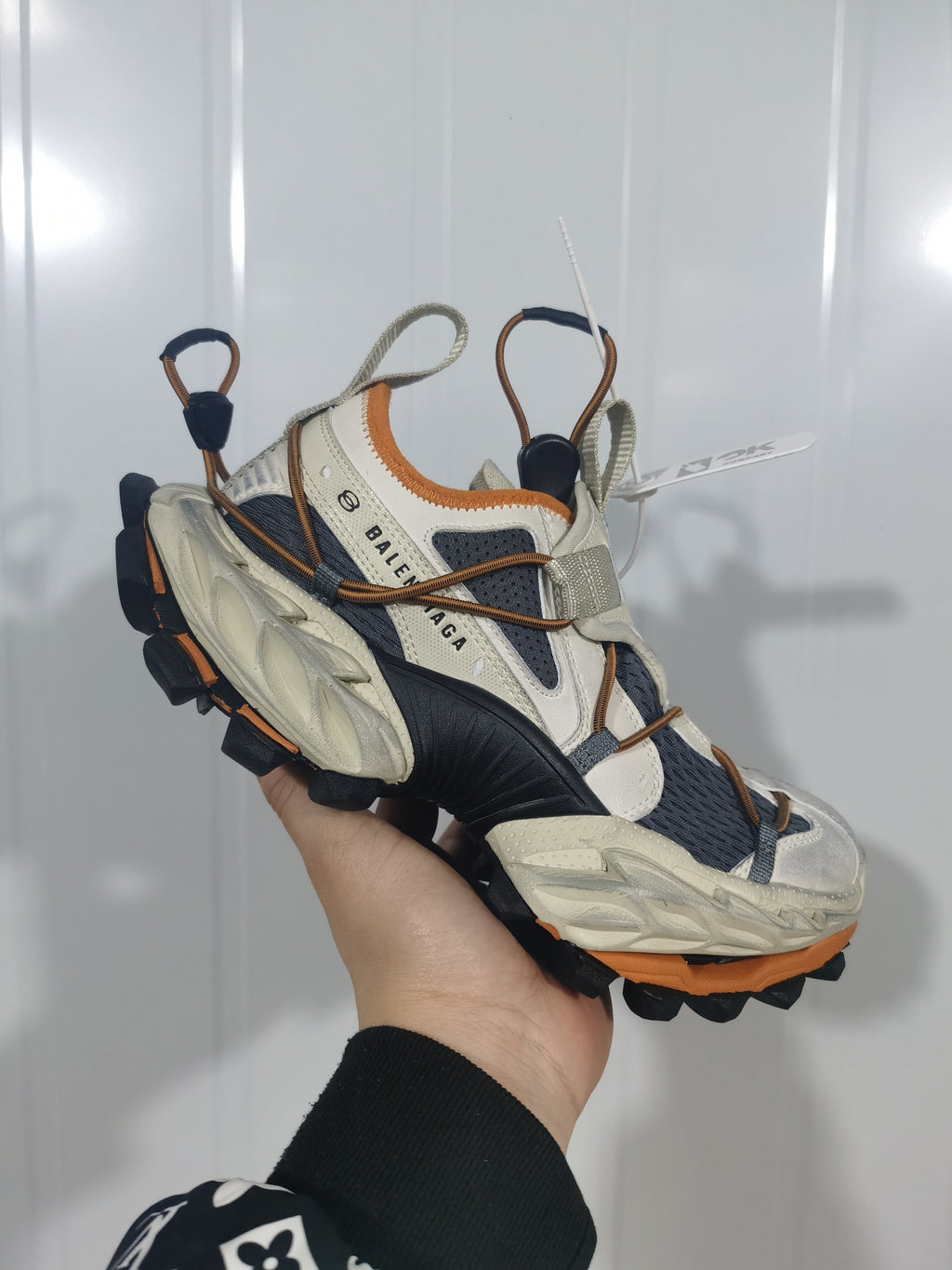 Close-up of a beige, black, and orange Balenciaga sneaker showing layered panels, cord-style lacing, gray webbing, and a sculpted sole.
