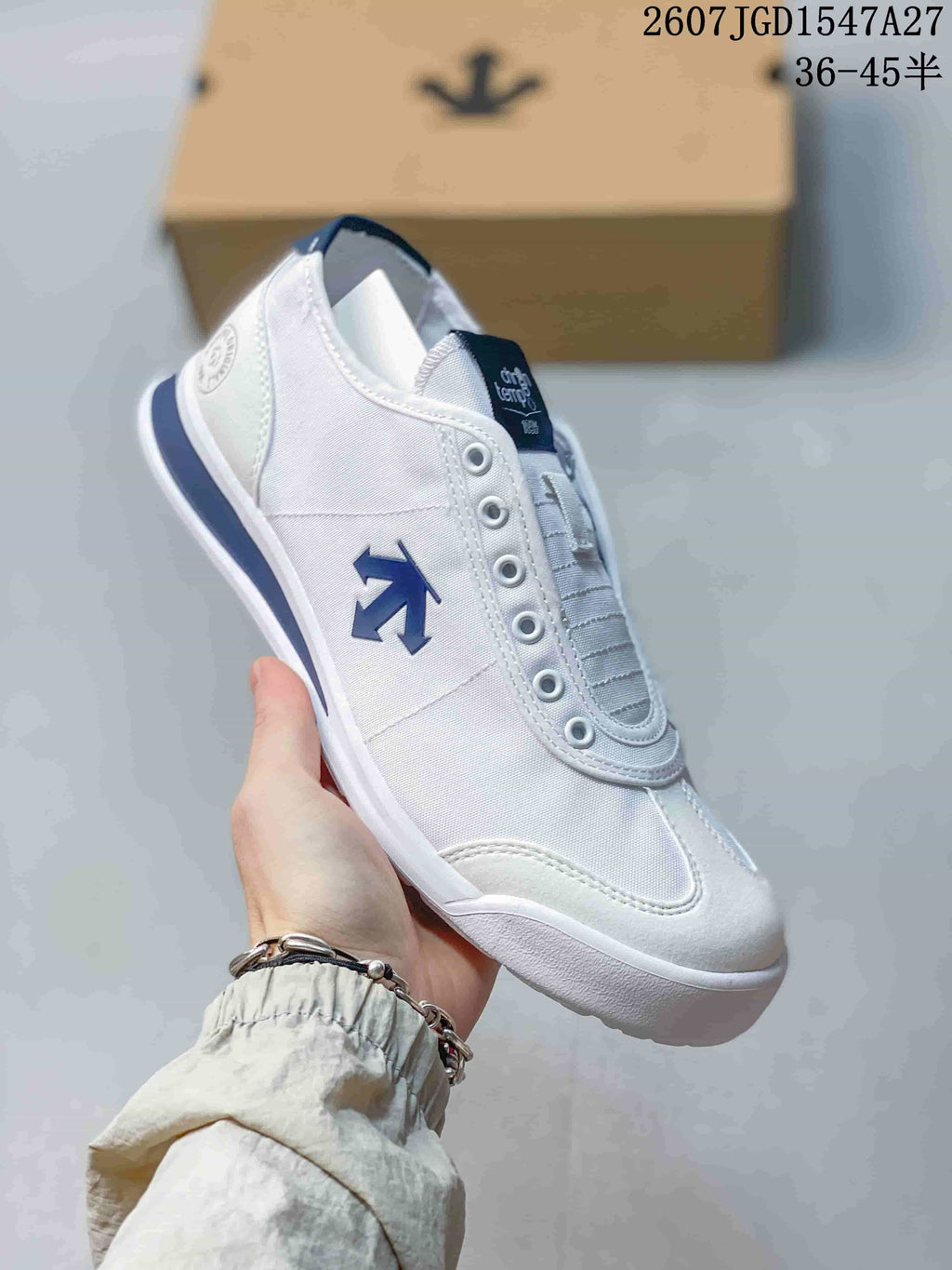 Angled side view of the white sneaker showing the blue side emblem, textile-looking upper, and white sole.