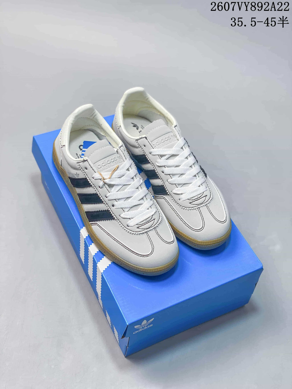 Pair of white low-top adidas sneakers with dark blue side stripes and gum-colored soles displayed on a blue shoebox.