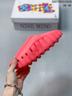 Side profile of the coral-red Nike Mind 001 mule showing perforations, openings, and the ridged outsole.