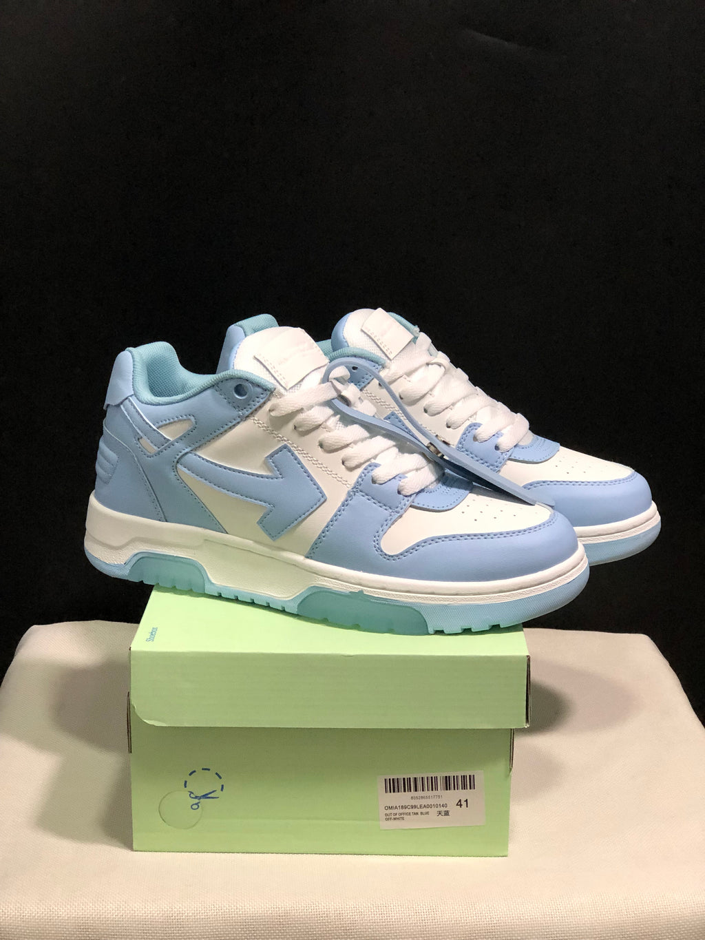 Pair of light blue and white OFF-WHITE Out Of Office low-top sneakers displayed on a green shoe box.