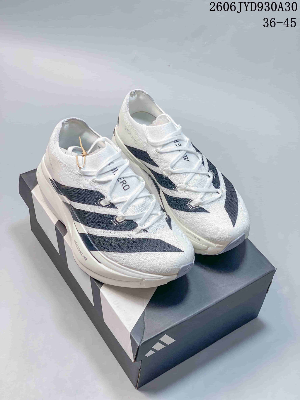 Pair of white adidas Adizero Prime X3 running shoes with dark stripes, shown from above on a box.