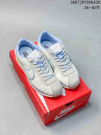 Pair of white Nike Classic Cortez sneakers with light blue accents displayed on a red shoe box.