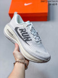 White Nike Vomero Plus running shoe with a light gray upper and visible ZoomX heel branding, photographed beside an orange shoe box.