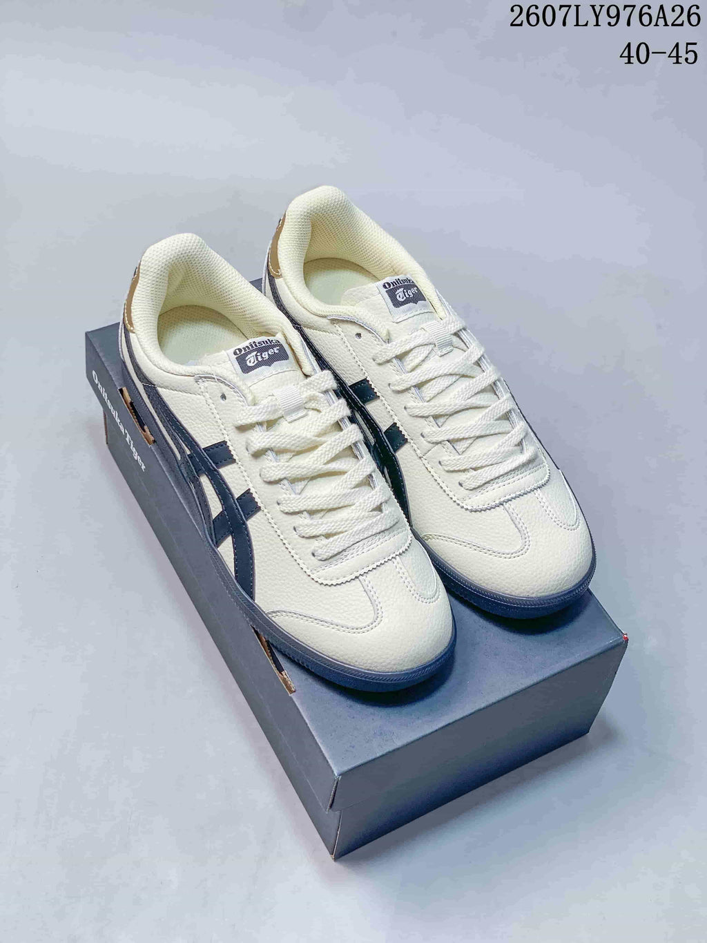 Off-white Onitsuka Tiger Tokuten sneakers with dark blue side stripes displayed on a shoebox.