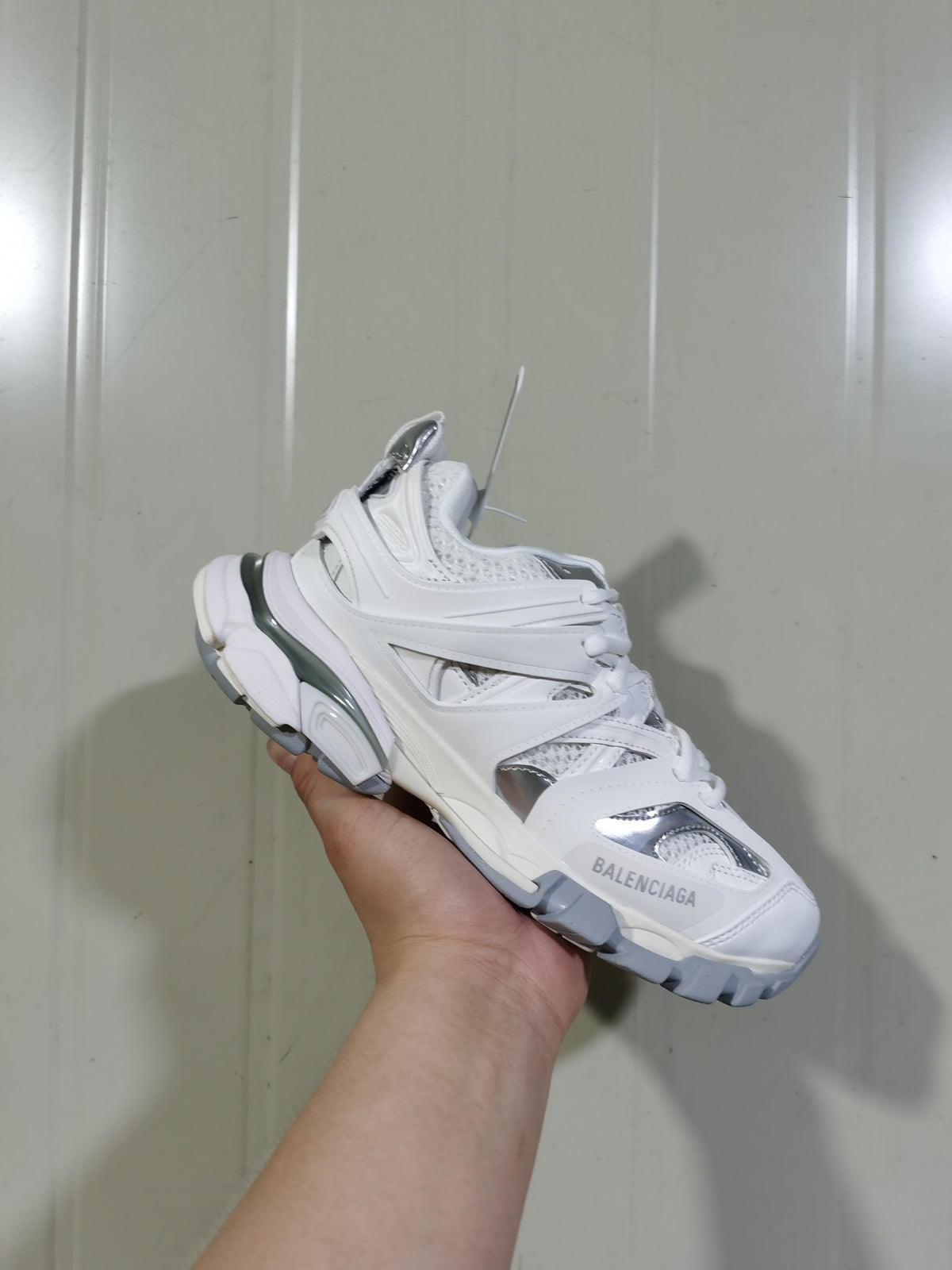Close angled view of the white and silver Track sneaker showing the lace-up front, layered upper, and branded toe panel.