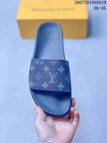 Top view of a navy monogram slide sandal with a wide patterned strap, raised sole, and a yellow box in the background.
