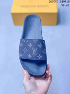 Top view of a navy monogram slide sandal with a wide patterned strap, raised sole, and a yellow box in the background.