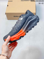 Side view of a charcoal-gray Salomon Ultra Glide 4 with orange midsole accents and a lugged outsole.