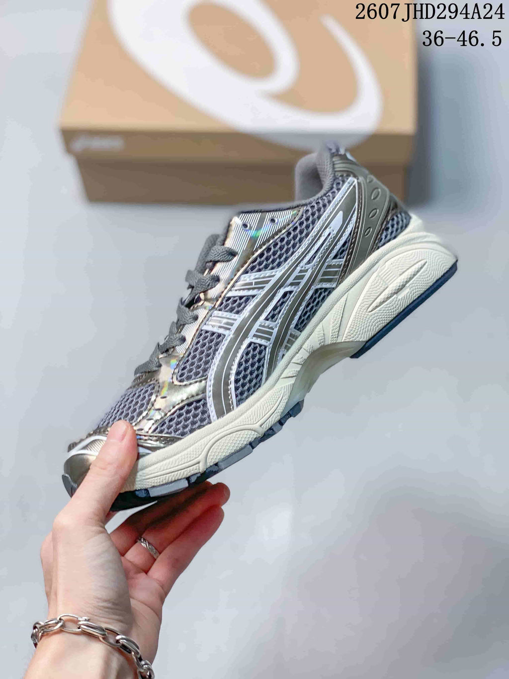 Side profile of the silver-gray sneaker showing mesh panels, metallic overlays, layered midsole construction, and a dark outsole; image text shows style code 2607JHD294A24 and size range 36–46.5.
