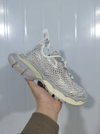 Angled close view showing the open mesh-style upper, reflective detailing, gray overlays, and segmented sole.