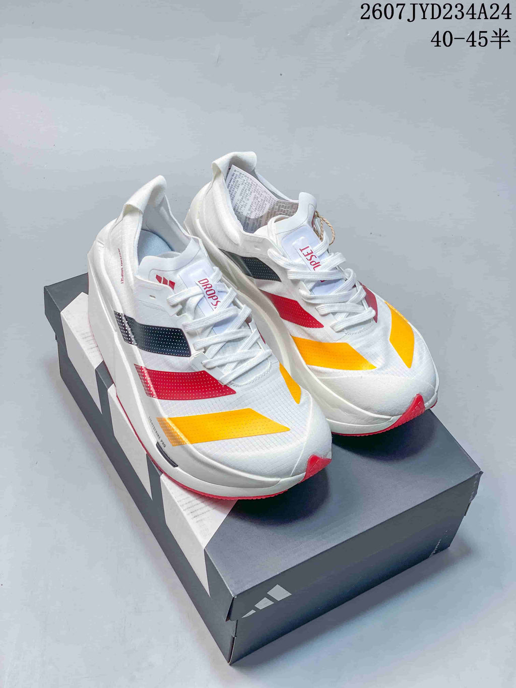 Pair of white adidas Dropset Elite running shoes with red, yellow and black accents displayed on a shoebox.