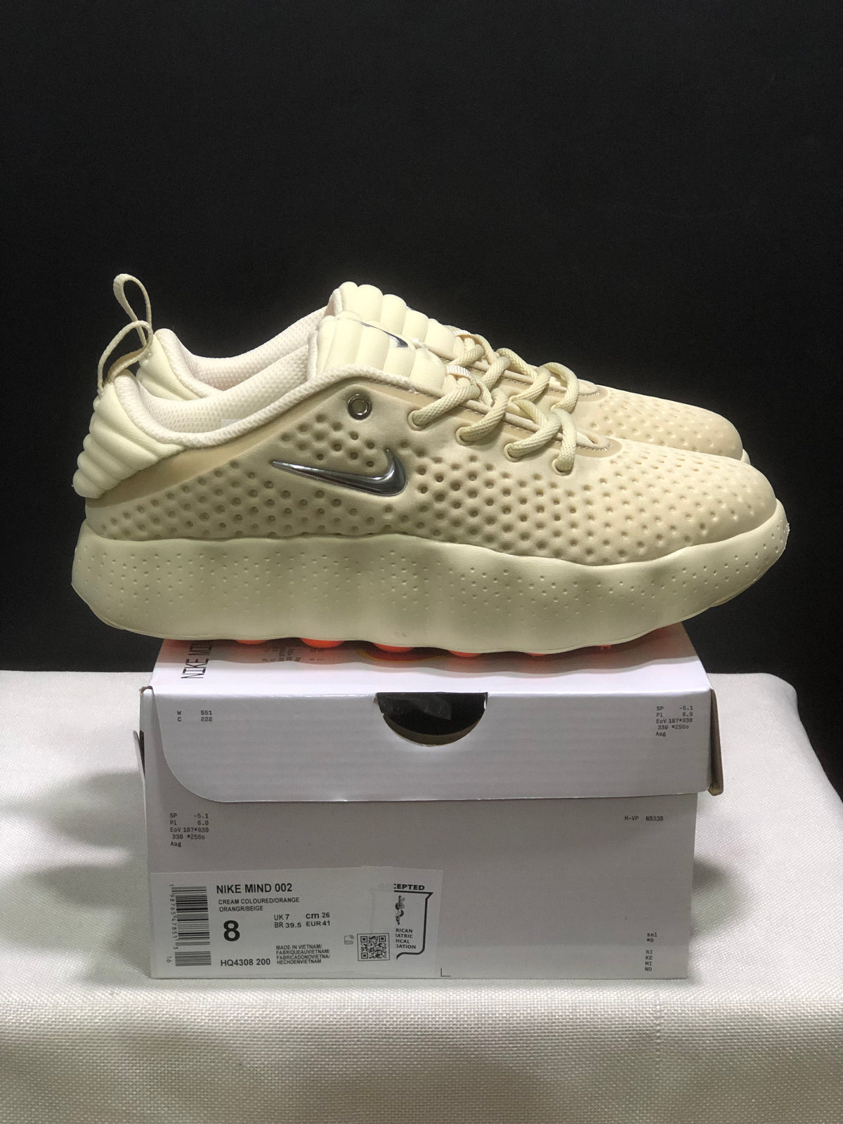 Side view of a cream Nike Mind 002 sneaker with padded collar, textured upper, silver branding, and sculpted sole.