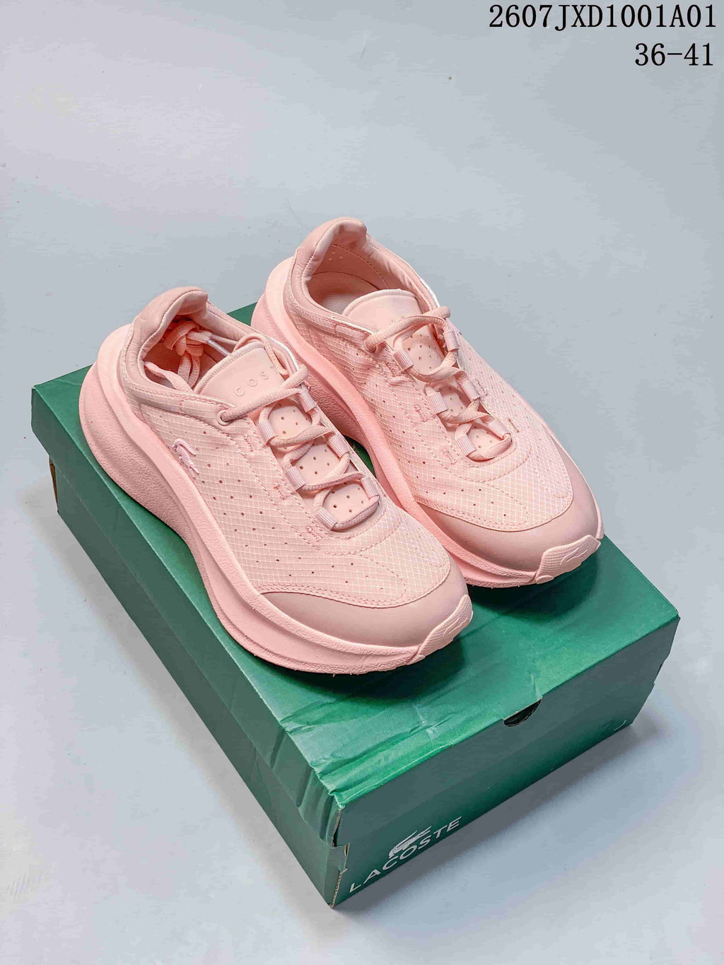 Pair of pink Lacoste lace-up sneakers displayed on a green shoe box