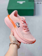 Angled side view showing the pink upper, orange accents, Lacoste emblem, and sculpted sole.