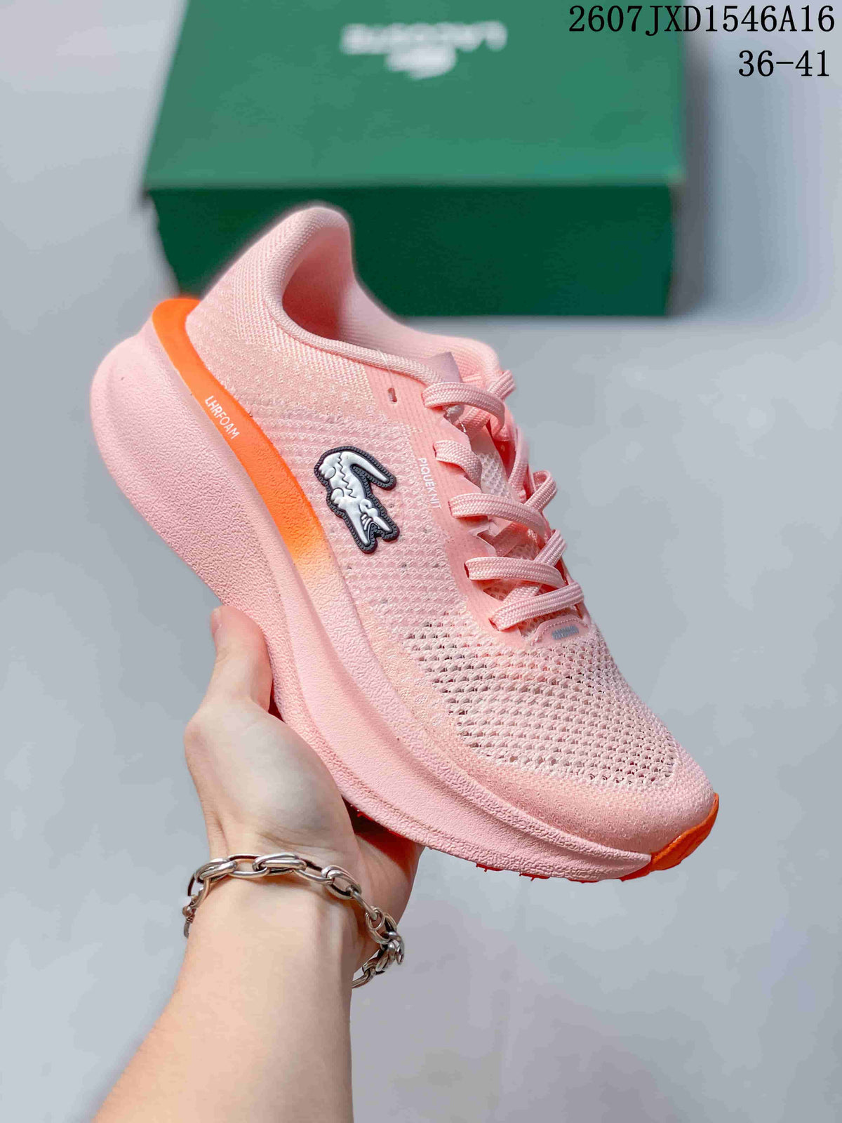Angled side view showing the pink upper, orange accents, Lacoste emblem, and sculpted sole.