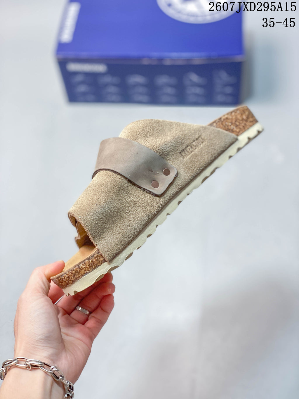 Side view highlighting the taupe suede upper, adjustable buckle strap, open heel and layered sole.