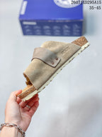 Side view highlighting the taupe suede upper, adjustable buckle strap, open heel and layered sole.