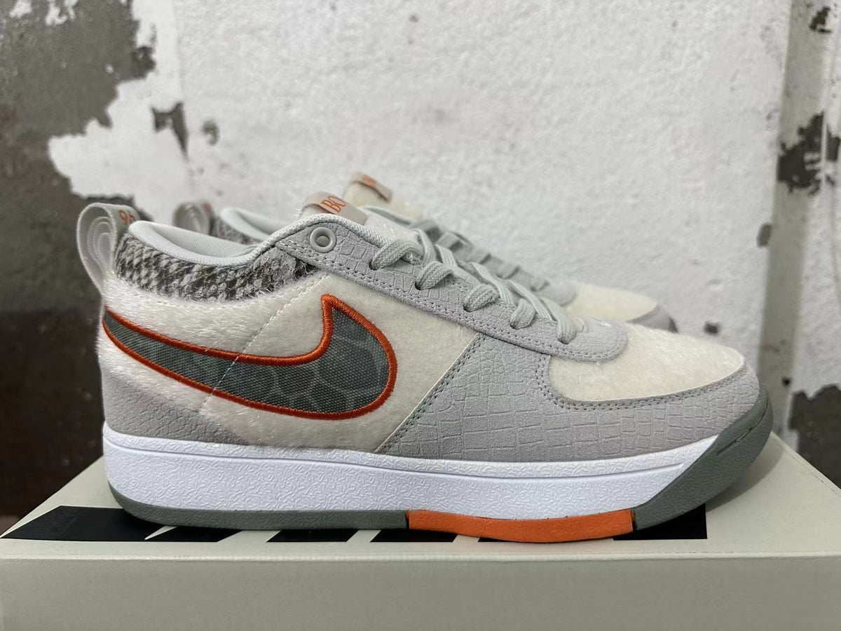 Side view of a Nike Book 1 sneaker with a dark swoosh outlined in orange.