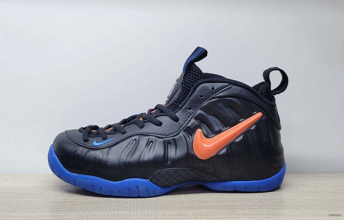 Side view of a black Nike Air Foamposite Pro sneaker with an orange Swoosh and blue outsole.