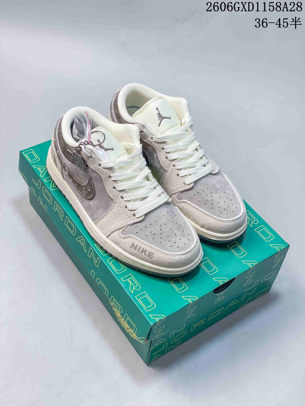 Pair of light grey and brown Air Jordan 1 low-top sneakers with white laces, a speckled Swoosh and detachable charm