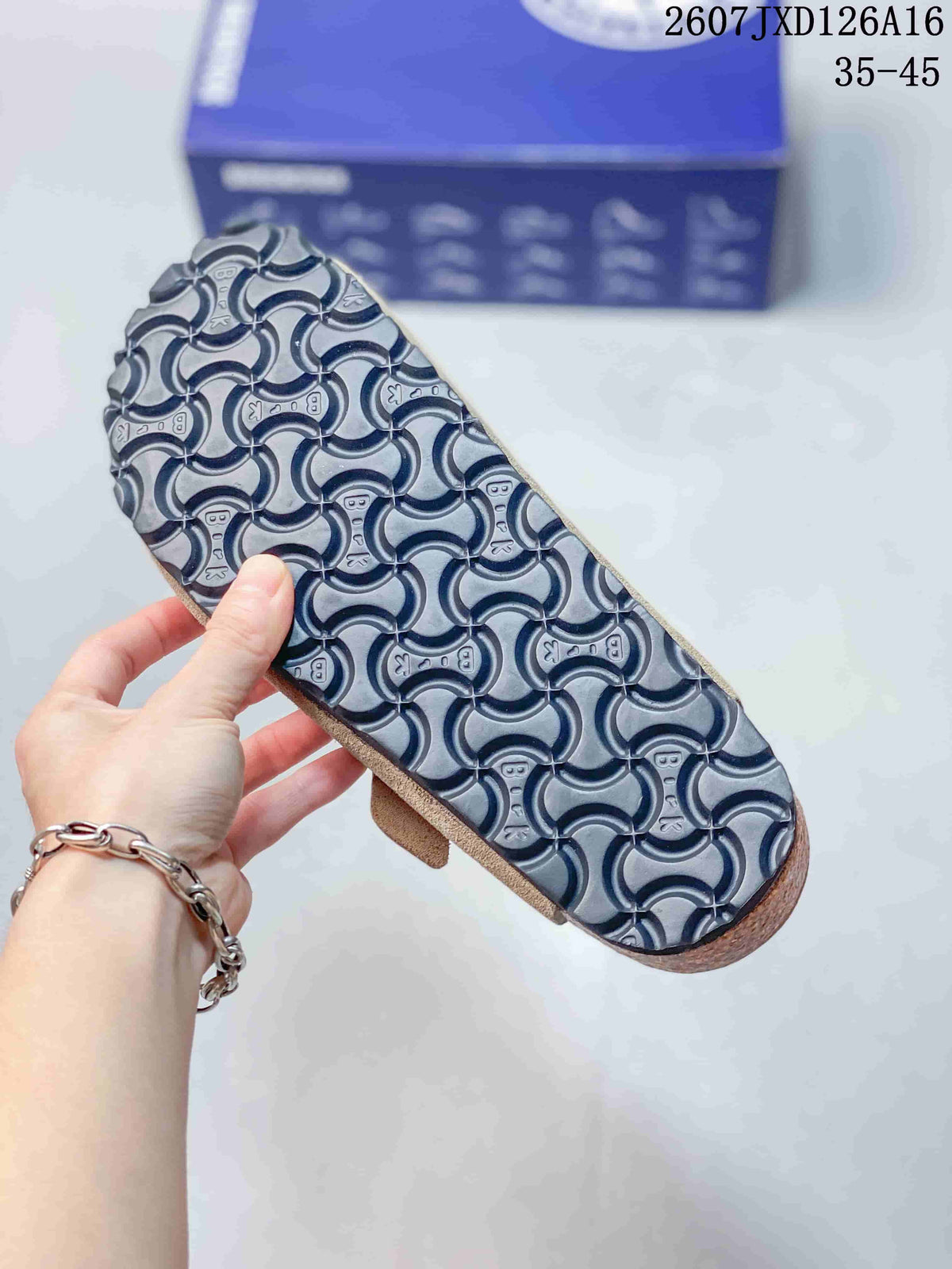 Close-up of the patterned black outsole on a taupe closed-toe mule, with a blue shoe box in the background.