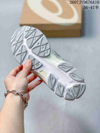 Bottom view of an ASICS sneaker showing the segmented gray-and-white outsole tread; a shoebox is in the background.