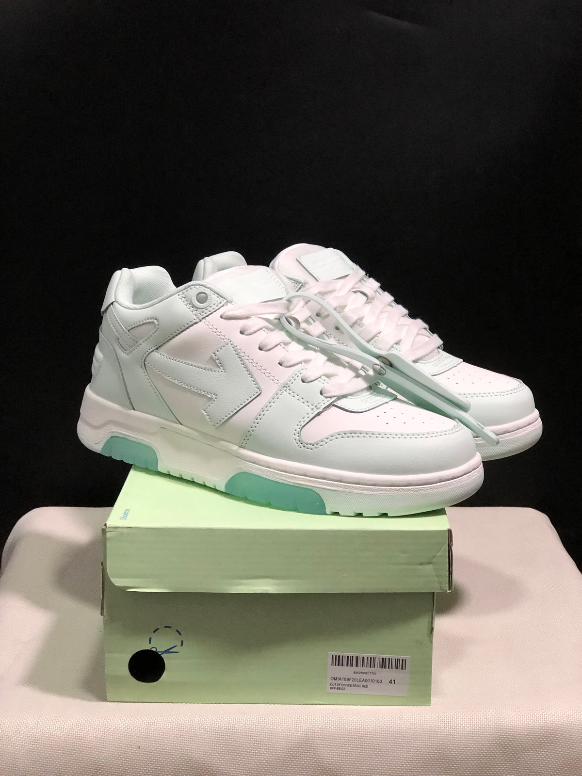 Pair of white Off-White Out Of Office low-top sneakers displayed on a pale green shoebox, showing mint outsole accents and attached lace accessories.