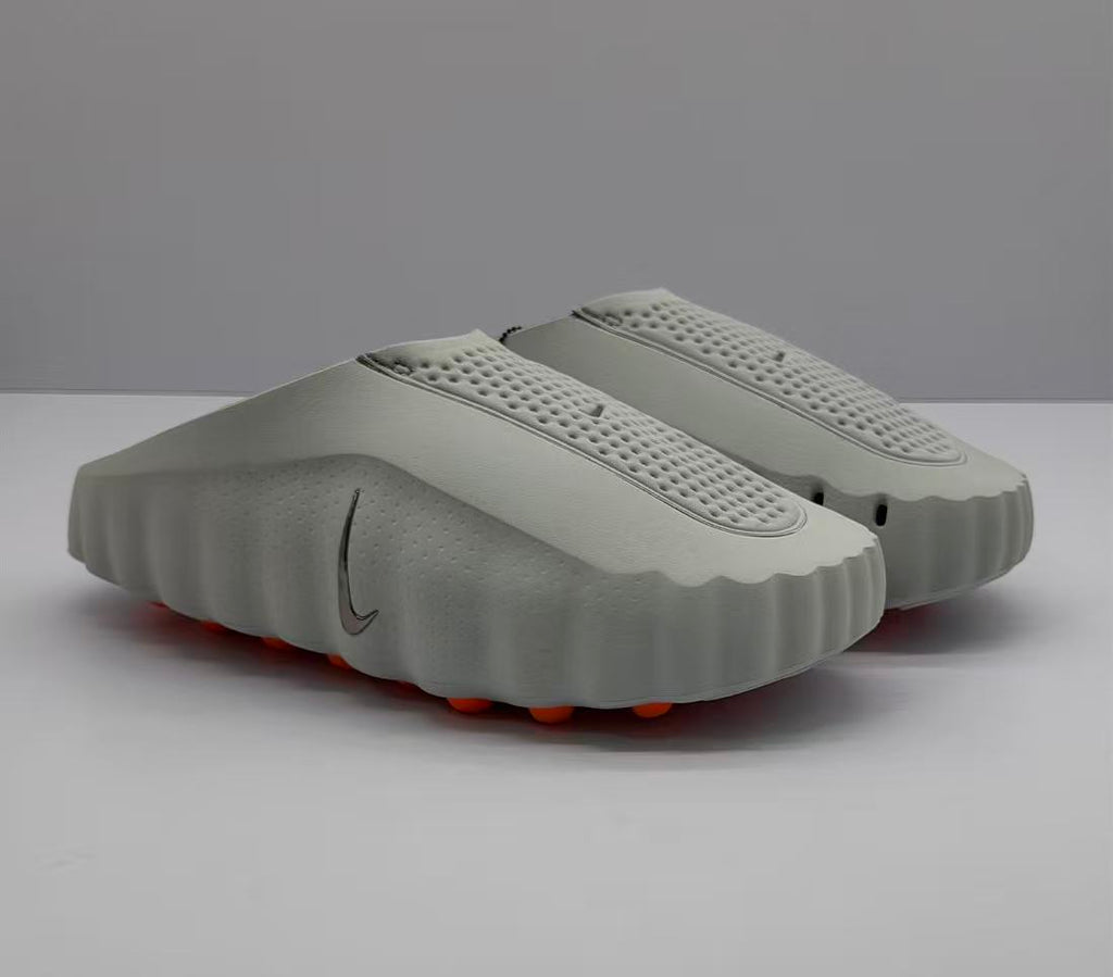 Three-quarter view of a pair of gray Nike slide sandals with perforated footbeds and orange outsole elements.