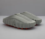Three-quarter view of a pair of gray Nike slide sandals with perforated footbeds and orange outsole elements.