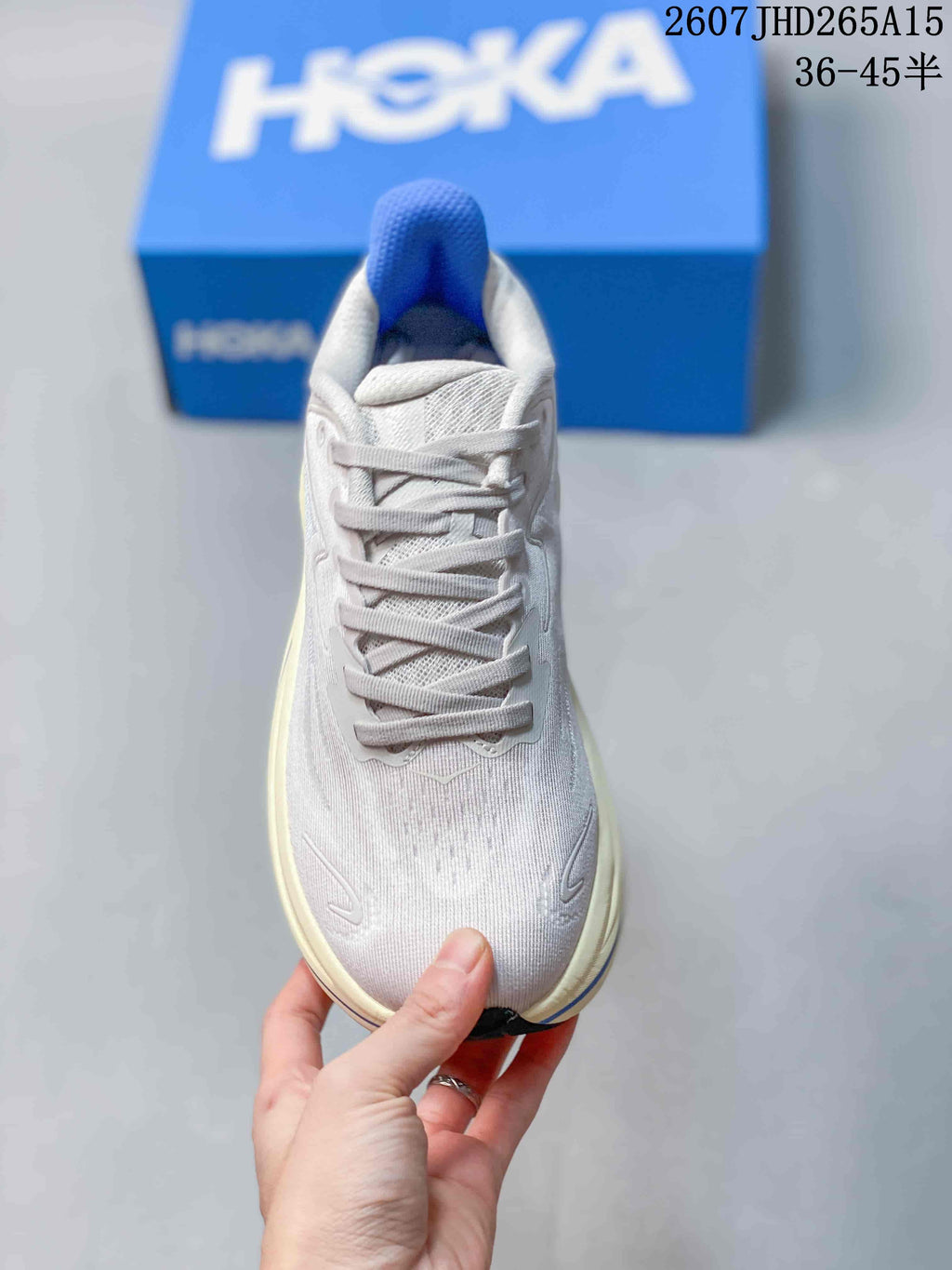 Top view of a light-colored lace-up HOKA Clifton 10 sneaker with a blue tongue detail.