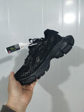 Black fishnet-style sneaker held at an angle, showing the textured upper, laces, and segmented sole.