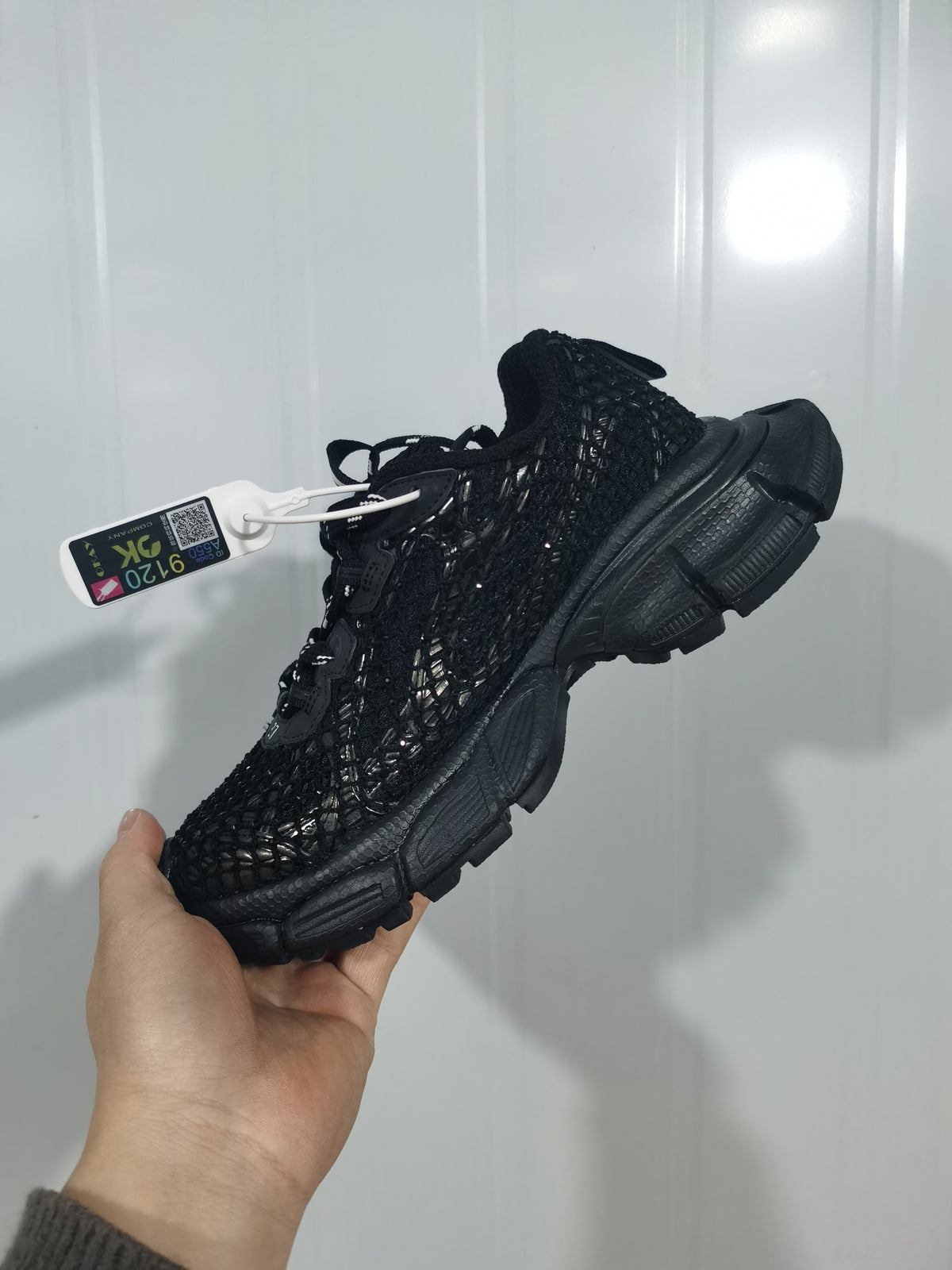 Black fishnet-style sneaker held at an angle, showing the textured upper, laces, and segmented sole.