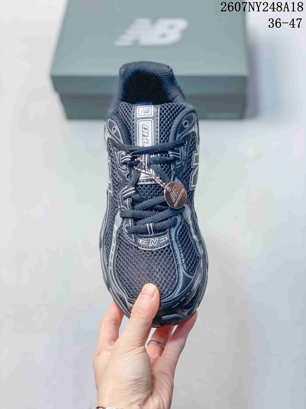 Front view of a black and gray lace-up sneaker showing the mesh toe box, tongue branding, and decorative lace tag.