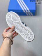 Close view of the white outsole showing a repeating zigzag tread pattern, with a blue Adidas shoebox in the background.