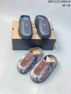 Front view showing black and gray slides on a box and brown multicolor slides in the foreground; image text shows style code 2607JJY1586A16 and size range 40–46.