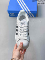 Top view of the white lace-up sneaker showing the tongue branding, shell-style toe texture, and black side stripes.
