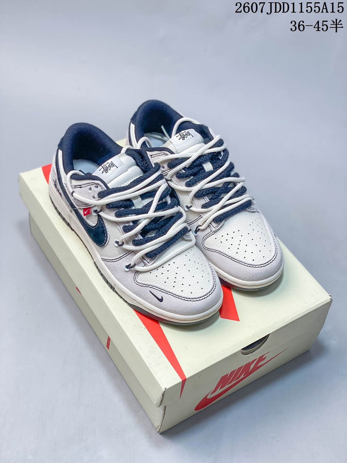 Pair of white low-top sneakers with navy accents, layered laces and graphic tongue details on a Nike shoe box.