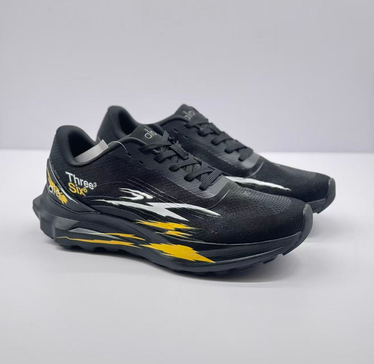 Three-quarter view of a pair of black Alo sneakers with contrasting white and yellow side graphics.