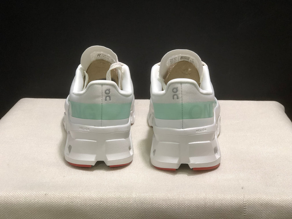 Rear view of the pair showing the On branding, pale green heel panels, padded collars, and red outsole accents.