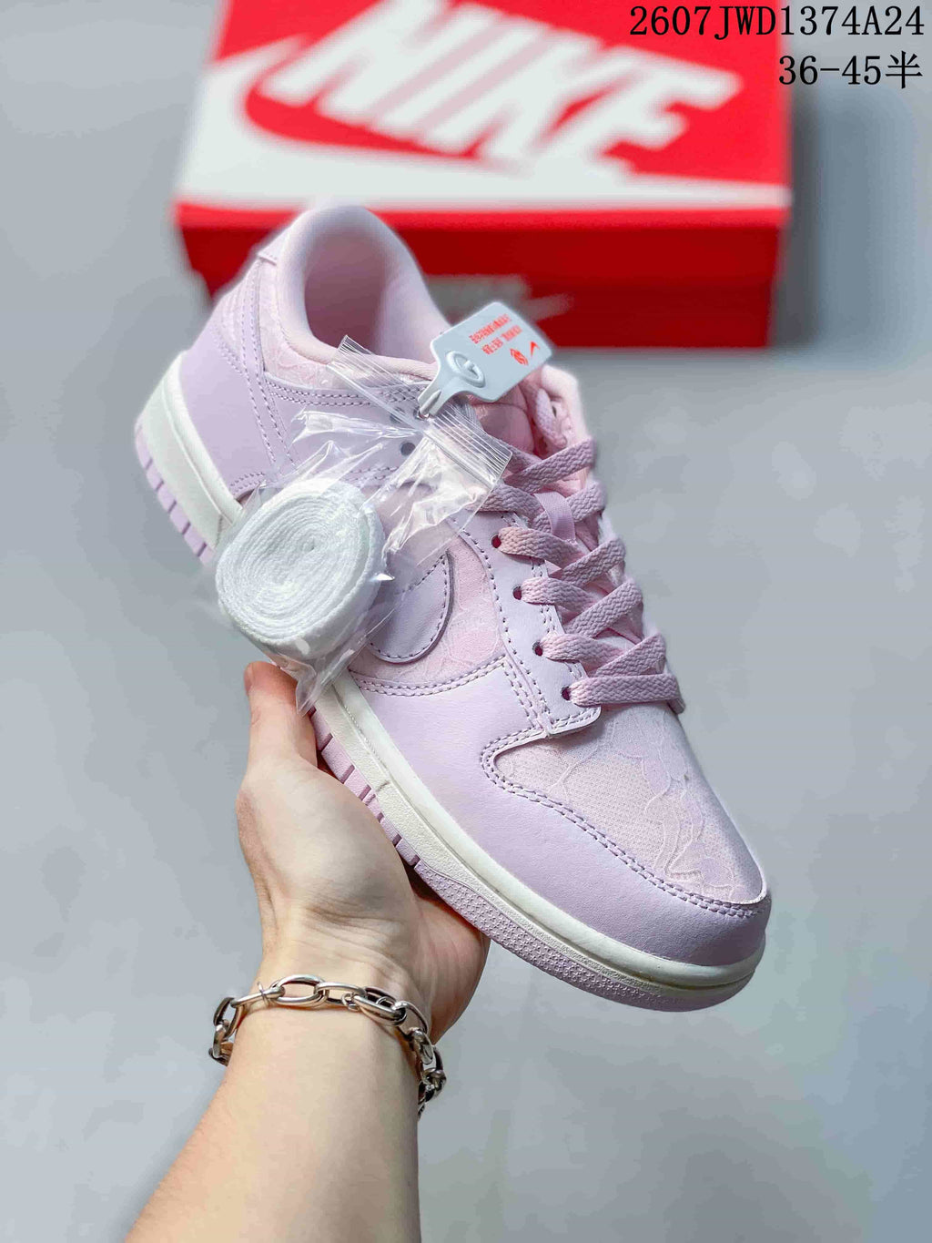 Angled side view showing the pink and lilac upper, Swoosh overlay, and spare laces.