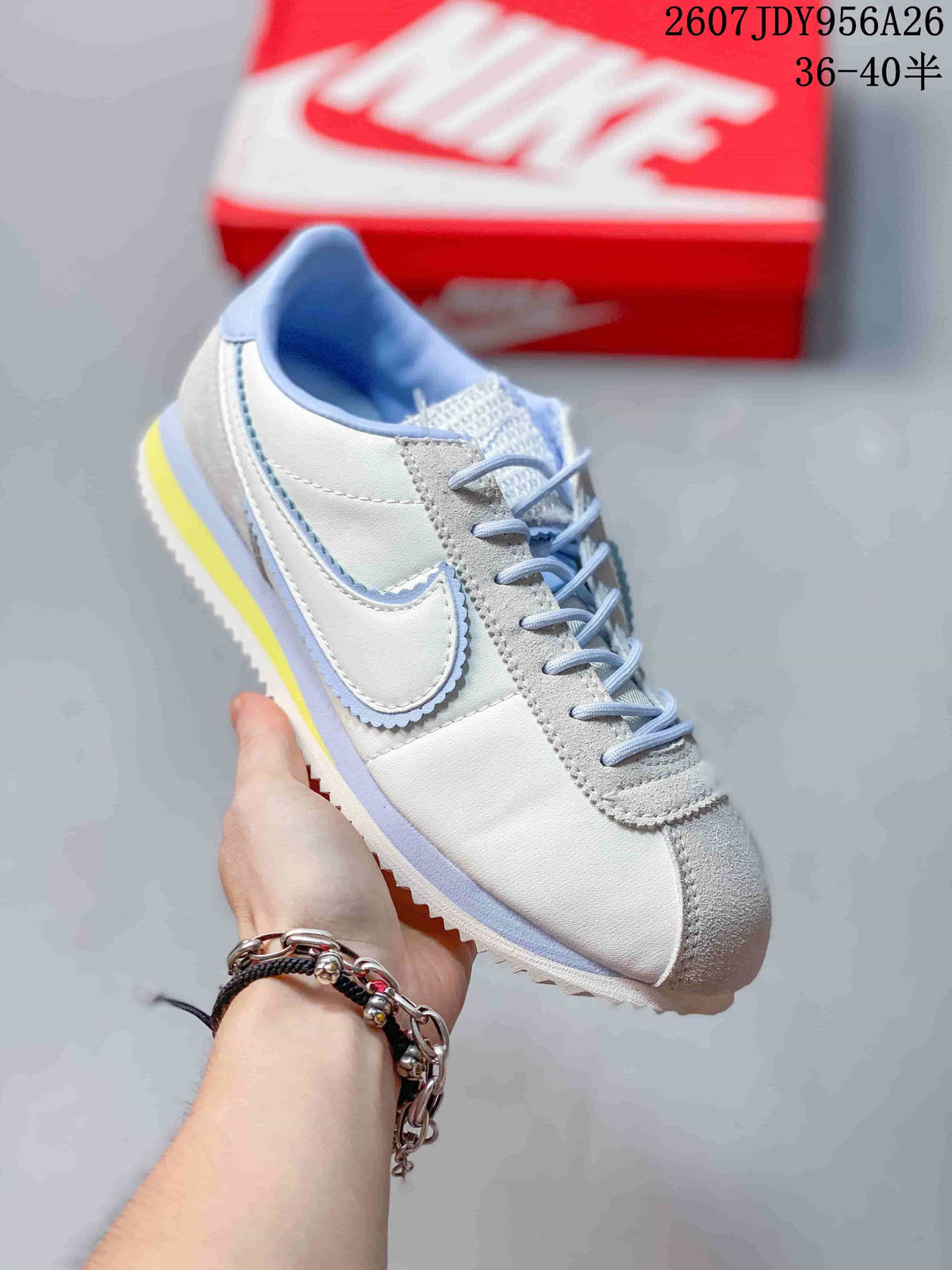 Close-up side view of a white Nike Classic Cortez sneaker showing the Swoosh, laces, padded collar and textured outsole; overlay text shows style code 2607JDY956A26 and size range 36–40.5.